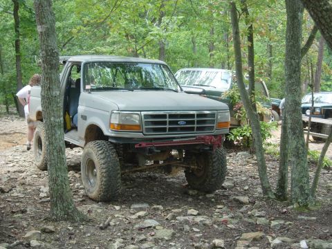 1995 Ford Bronco - A lifted 1995 Ford Bronco is seen off-roading with other vehicles in a wooded area.