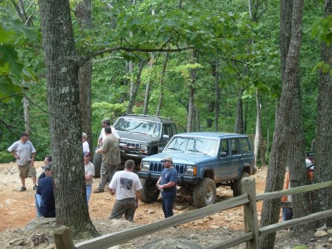 1995 Ford Bronco - Two SUVs are parked on a dirt path in a wooded area with several people around them.