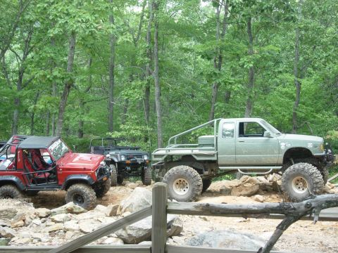 1995 Ford Bronco - Several off-road vehicles are parked on a rocky trail surrounded by trees.