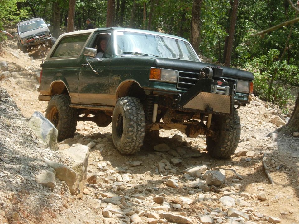 Green Ford Bronco on a rocky trail, another SUV behind it