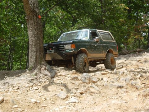 1995 Ford Bronco - A modified Ford Bronco navigates a challenging off-road trail with large rocks and steep inclines.