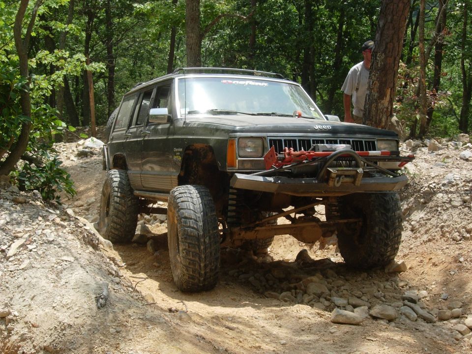 Dark green Jeep Cherokee with off-road modifications on a rocky trail