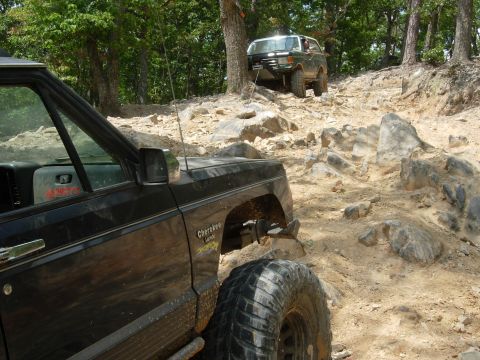 1995 Ford Bronco - Two off-road vehicles navigate a challenging rocky trail, with one Jeep Cherokee in the foreground and another SUV ahead.