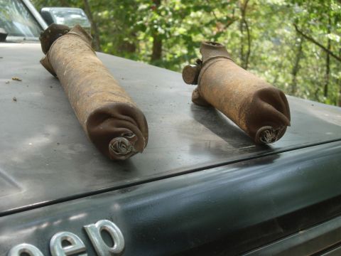 1995 Ford Bronco - Two old, rusty exhaust pipes are resting on the hood of a dark-colored Jeep.