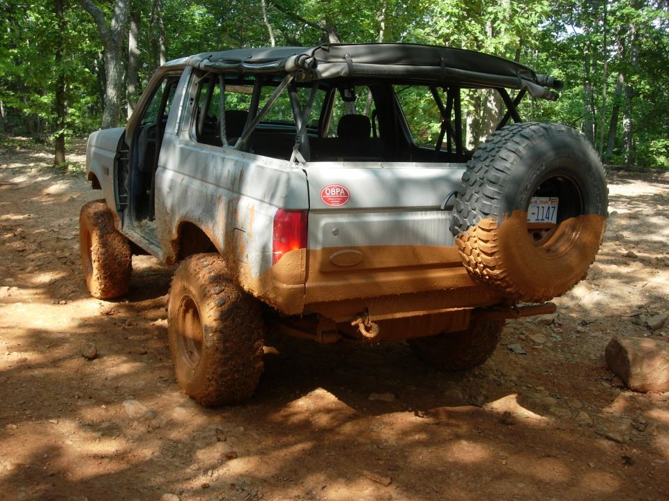 Mud-covered Ford Bronco with spare tire on rear, soft top removed, off-road tires