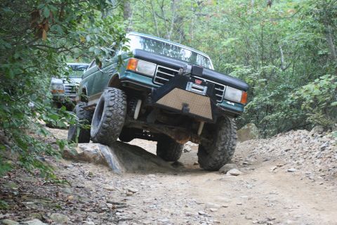 1990 Ford Bronco - A modified green Ford Bronco tackles a challenging off-road course, with another vehicle visible behind it.