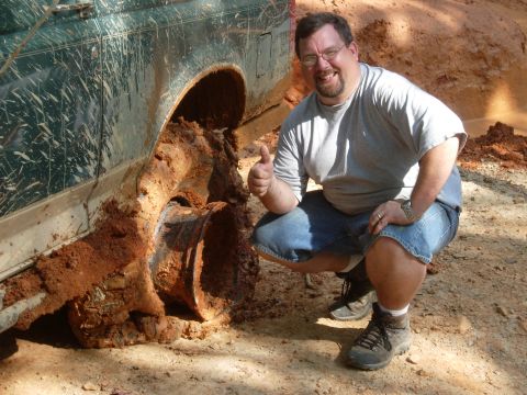 1995 Ford Bronco - A 1995 Ford Bronco is deeply stuck in mud, with a man giving a thumbs-up gesture next to it.