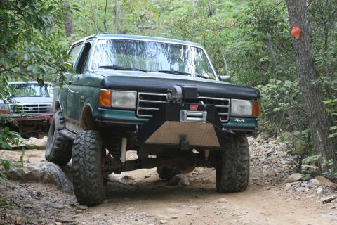 1990 Ford Bronco - This modified SUV navigates a challenging off-road path through a wooded area.