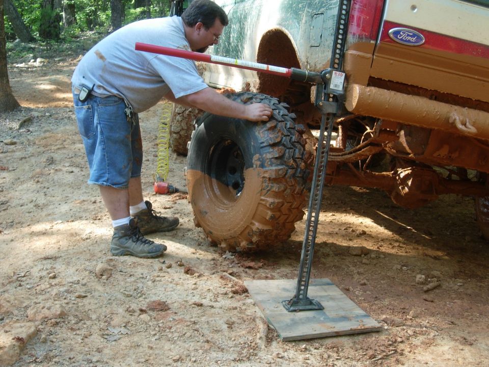 Red 1995 Ford Bronco side view, man jacking up muddy tire