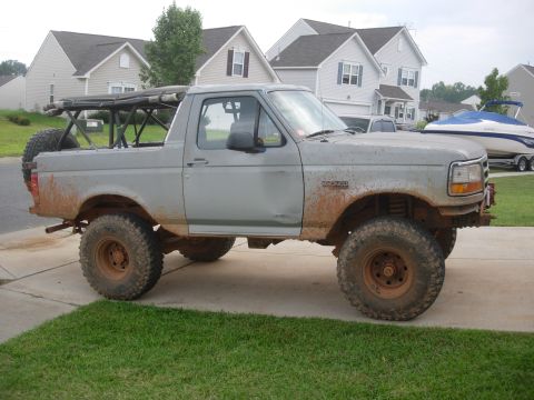 1995 Ford Bronco - This lifted Ford Bronco is shown from the side, equipped with a roll cage and off-road tires.