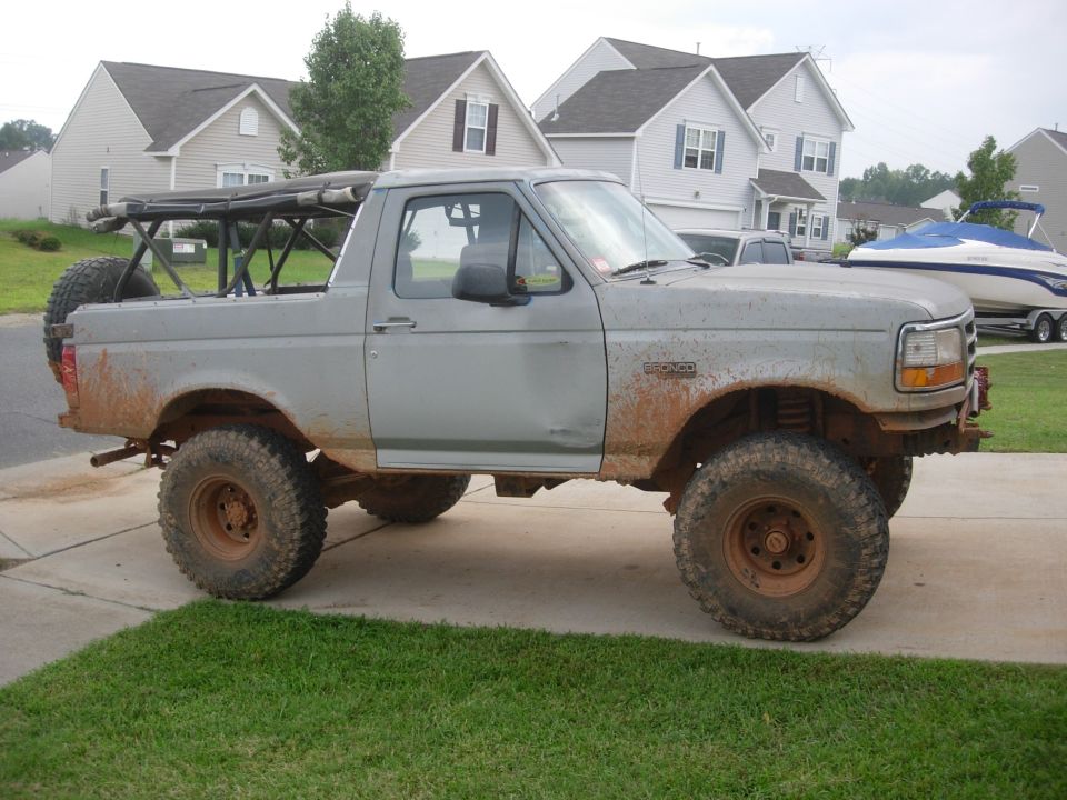 Gray Ford Bronco with a roll cage and spare tire, lifted with off-road tires, covered in mud