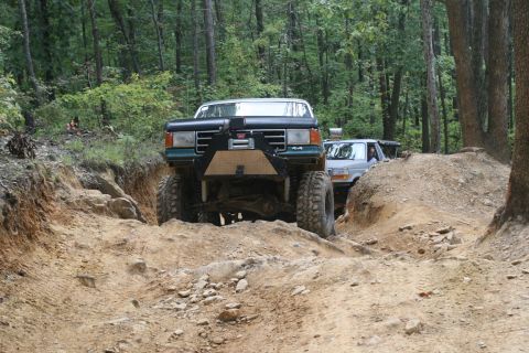 1990 Ford Bronco - A modified 1990 Ford Bronco navigates a challenging off-road trail, with another vehicle following behind.