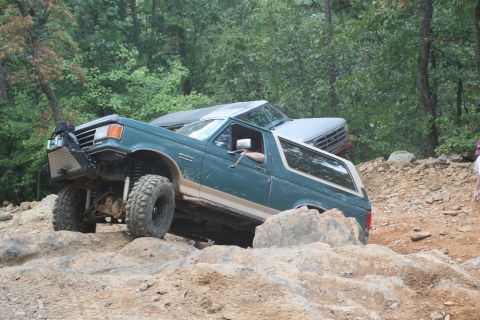 1990 Ford Bronco - A green 1990 Ford Bronco navigates a challenging rocky trail, with another vehicle visible behind it.