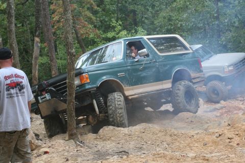 1990 Ford Bronco - A green 1990 Ford Bronco tackles a challenging off-road course, with another vehicle visible behind it.