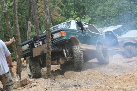 1990 Ford Bronco - Two off-road vehicles tackle a challenging dirt path with steep inclines and obstacles.