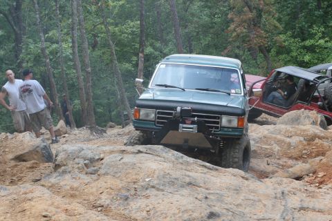 1990 Ford Bronco - Two off-road vehicles navigate a challenging rocky trail in a wooded area.