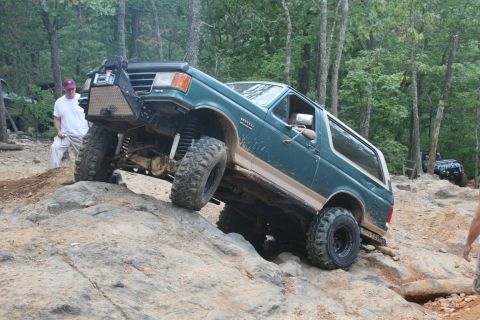 1990 Ford Bronco - A green 1990 Ford Bronco tackles a challenging off-road course with another vehicle visible in the background.