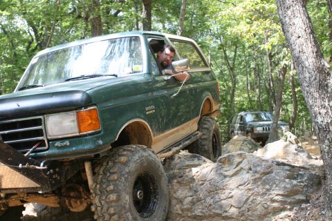 1990 Ford Bronco - Green 1990 Ford Bronco tackling a challenging off-road trail with a second vehicle following.