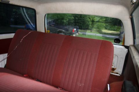 1987 Ford Bronco - The interior of an older vehicle shows a red bench seat and a view of a pickup truck through the rear window.