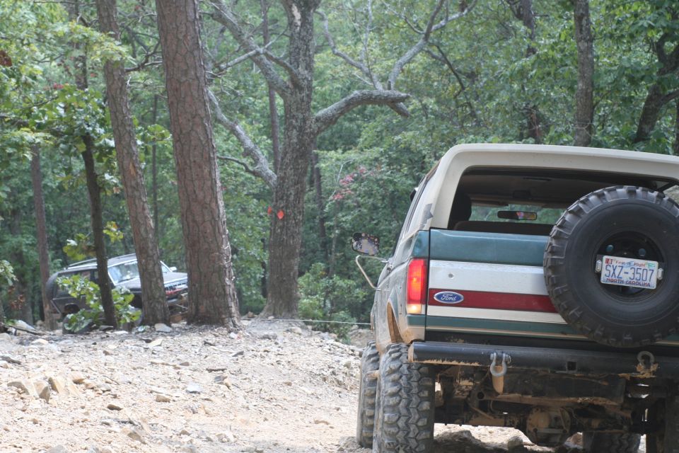 1990 Ford Bronco with spare tire on back, driving on dirt trail with another vehicle behind