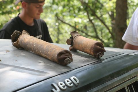 1990 Ford Bronco - Two rusty driveshafts rest on the hood of a Jeep, with a person blurred in the background.