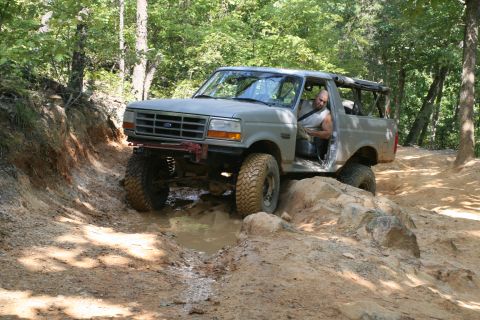 1990 Ford Bronco - A gray Ford Bronco navigates a muddy and rocky off-road trail.