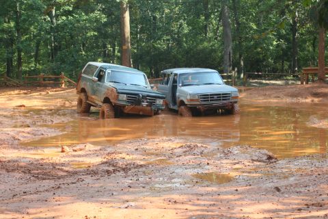 1990 Ford Bronco - Two SUVs, including a 1990 Ford Bronco, are stuck in a muddy off-road course.