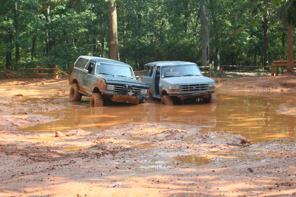 Green 1990 Ford Bronco and gray SUV stuck in mud