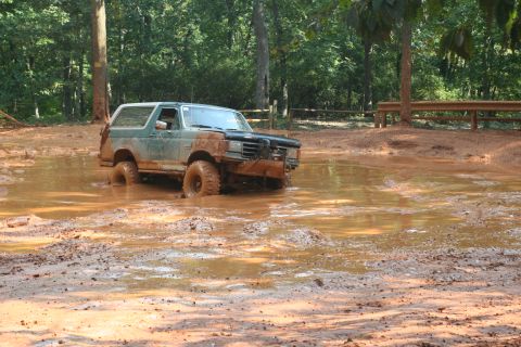 1990 Ford Bronco - Ford Bronco navigating a muddy obstacle course, tires deep in the mire.