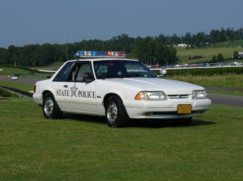 1993 Ford Mustang - A white 1993 Ford Mustang police car is parked on a grassy area next to a racetrack.