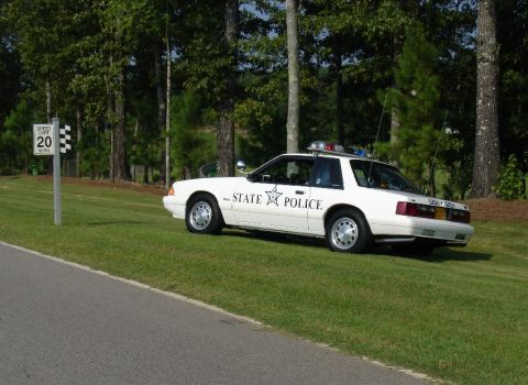 1993 Ford Mustang - A white 1993 Ford Mustang, marked "STATE POLICE", is parked on a grassy area next to a road.
