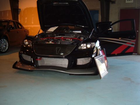 1991 Ford Probe - A black sports car is displayed indoors with its hood and driver's door open, revealing the engine bay and custom graphics.