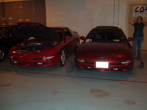 1991 Ford Probe - Two red Ford Probes are parked indoors, with one having its hood open to reveal the engine compartment.