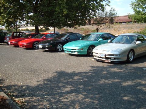 1991 Ford Probe - Several Ford Probe models are parked in a lot under trees, with a train track in the background.