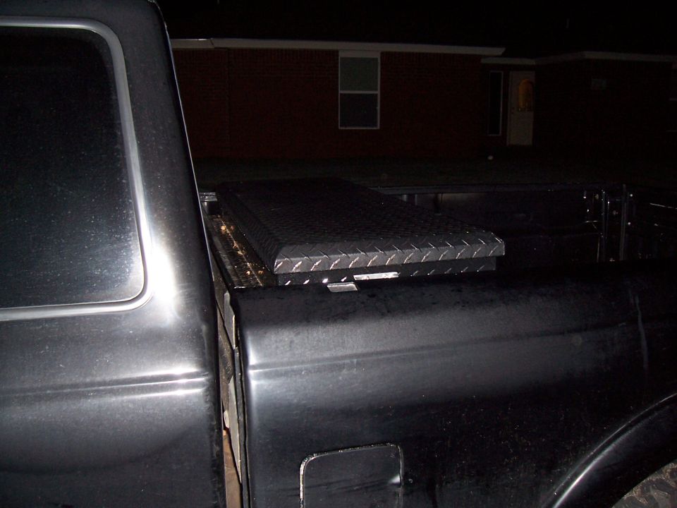 Diamond plate toolbox mounted in the bed of a dark-colored pickup truck