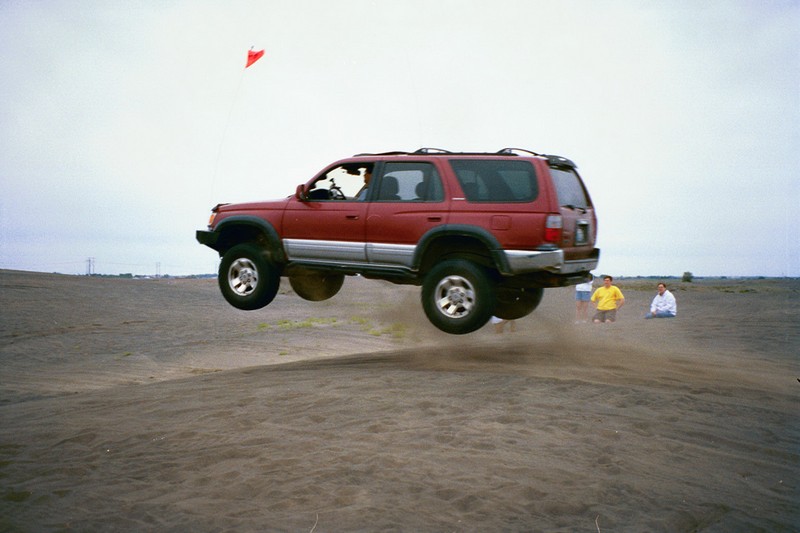 1996 Toyota 4Runner airborne over sand, two people watch in the background