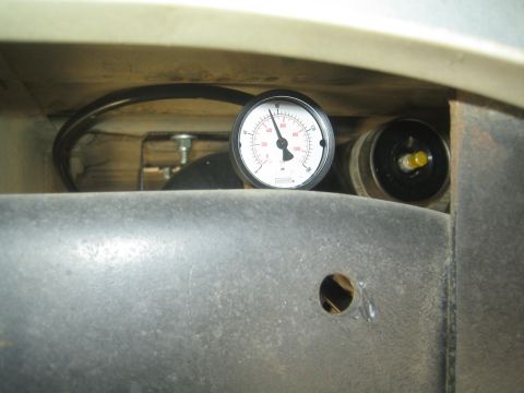 1990 Ford Bronco - round white-faced pressure gauge mounted in a tight space behind a metal vehicle panel.