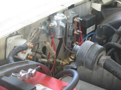 1990 Ford Bronco - solenoid, stacked relays and heavy battery cabling mounted along the firewall of an engine bay.