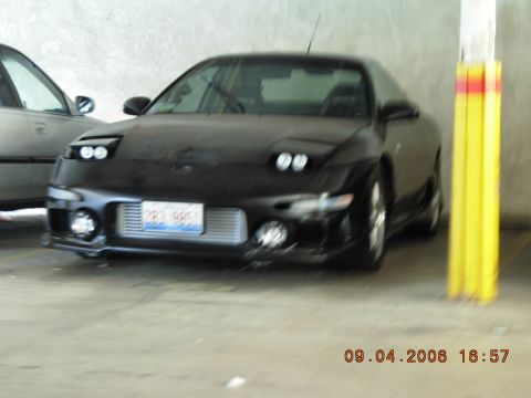 1993 Ford Probe - A black sports coupe is parked next to another vehicle, with a yellow and red striped pole to its right.