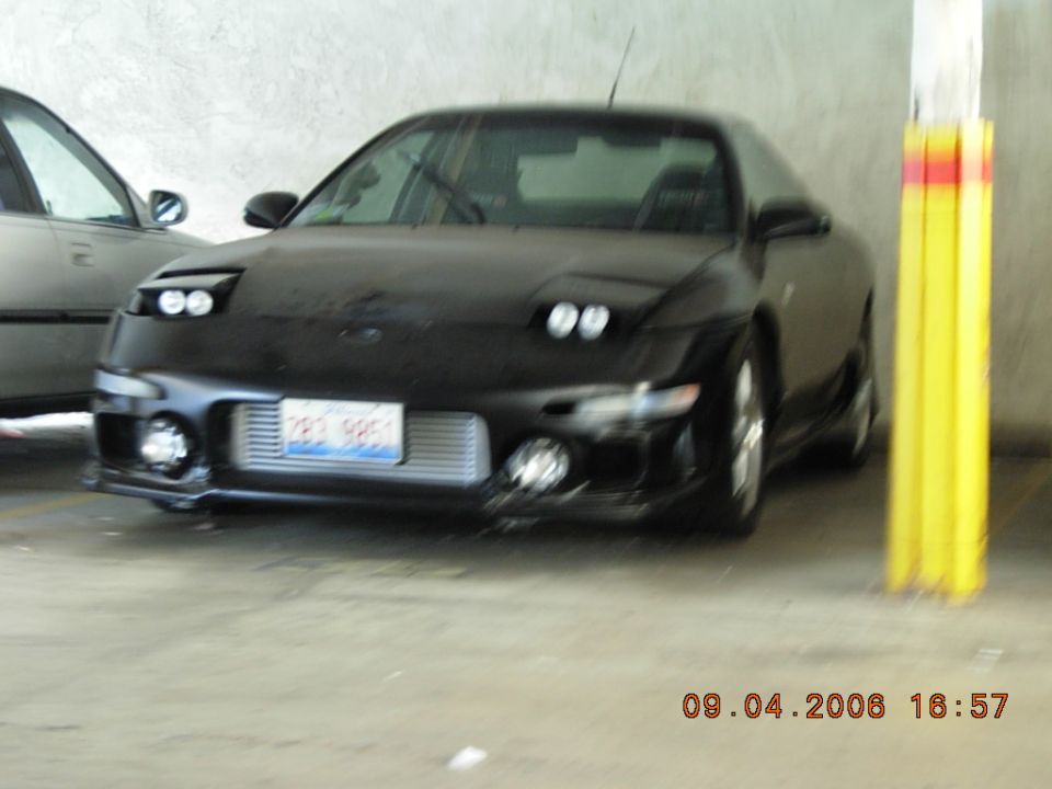 Black sports coupe with pop-up headlights and an intercooler visible behind the front license plate