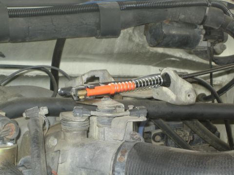 1990 Ford Bronco - orange spring-loaded valve or actuator mounted in a dusty engine bay surrounded by rubber hoses and wiring.