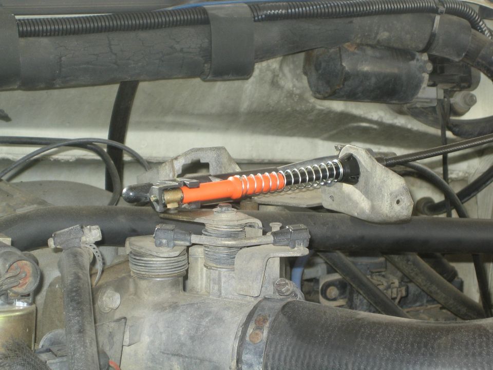 Orange spring-loaded air valve mounted on engine bay component with hoses