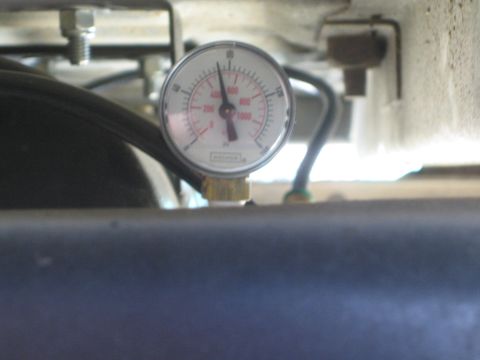 1990 Ford Bronco - round dual-scale pressure gauge with a red dial reading near zero, mounted below a blue cylindrical air tank.