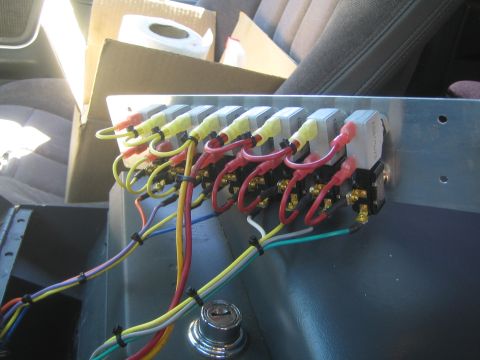 1990 Ford Bronco - bank of relays mounted on an aluminum panel with yellow, red and white wires, sitting inside a vehicle cabin.