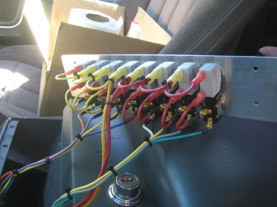 Row of electrical relays on aluminum panel with colorful wiring inside vehicle