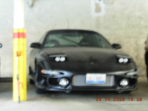 1993 Ford Probe - A black sports car is parked indoors, showing its front end with pop-up headlights and an exposed intercooler.