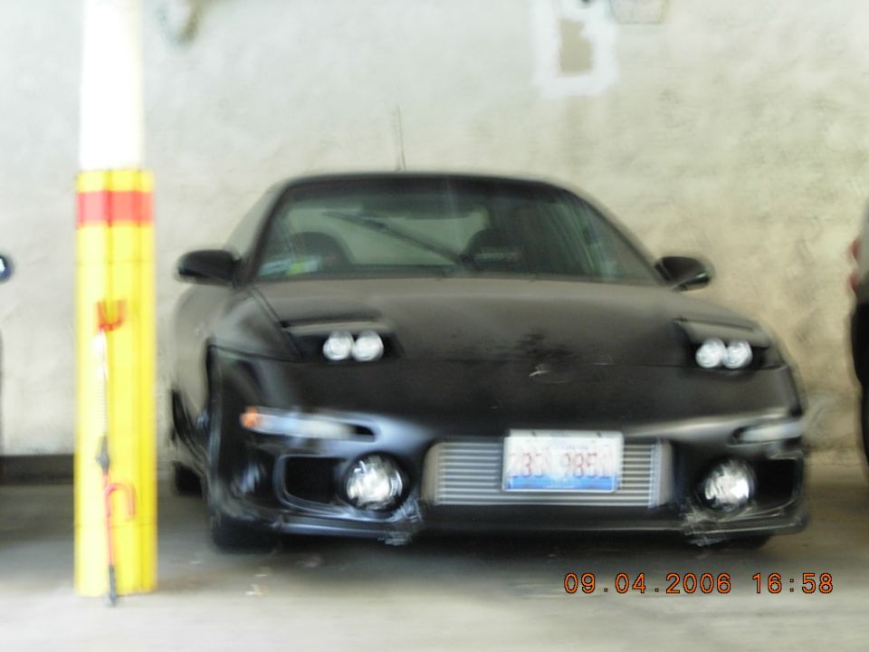 Blurry front view of a black coupe parked in a concrete garage next to a yellow column.