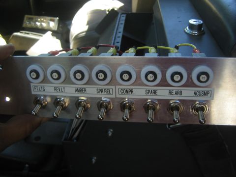 1990 Ford Bronco - aluminum control panel with eight labeled toggle switches (FT.LTS, REV.LT, AMBER, etc.) and pilot lights, held by hand.