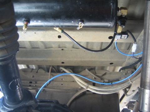 1990 Ford Bronco - Underbody view of a black air reservoir tank with brass ports and routed blue and black air lines along the frame.