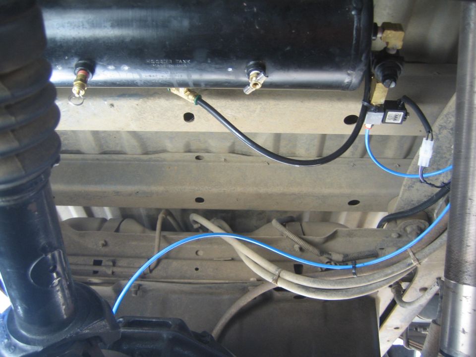 Underbody view of black air tank with fittings and routed blue air lines